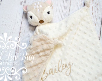 May include: A cream-colored security blanket featuring a plush deer head with embroidered facial details and a textured dimpled fabric surface. The blanket is personalized with the name Bailey embroidered in a cursive brown script font.