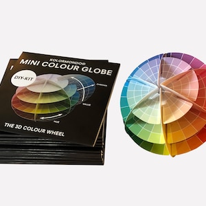 May include: A black and white DIY kit for a mini color globe. The kit includes a color wheel with the words "DIY-KIT", "The 3D Color Wheel", "KOLORMUNDO", "MINI COLOUR GLOBE", "HUE", "VALUE", and "CHROMA". The kit also includes a color globe that is assembled and shows the colors of the color wheel.