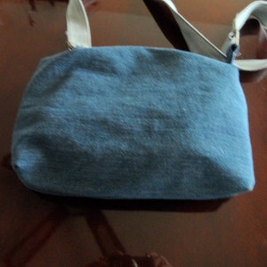 May include: A blue denim crossbody bag with a light gray strap. The bag has a simple design and is made of a soft, durable material.