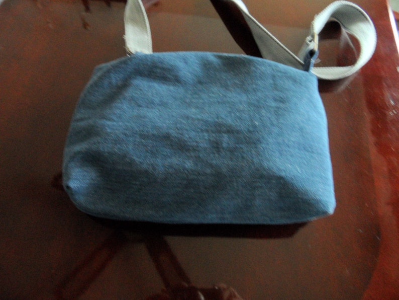 May include: A blue denim crossbody bag with a light gray strap. The bag has a simple design and is made of a soft, durable material.