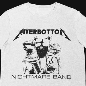 May include: A light gray t-shirt featuring a black and white graphic of three Muppet-like characters. The text "RIVERBOTTOM" is above the characters, and "NIGHTMARE BAND" is below.
