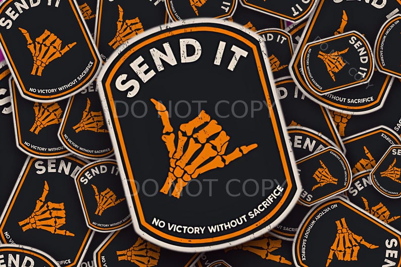 May include: Black sticker with the words "SEND IT" in white, featuring an orange skeleton hand in the shaka gesture. The phrase "NO VICTORY WITHOUT SACRIFICE" is printed below the hand.