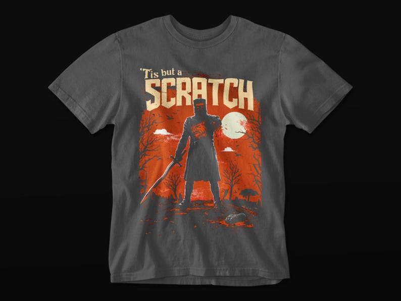 May include: Dark gray t-shirt featuring a graphic of a knight with a sword, standing in front of a red and orange background with a full moon. The text "'Tis but a SCRATCH" is above the knight.
