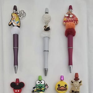 以下が含まれることがあります： 様々なデザインの装飾ペンコレクション。デザインには、不思議の国のアリス、白鳥、虹、ミッキーマウス、カエル、アヒル、ハイランド牛が含まれます。ペンは様々な色があります。