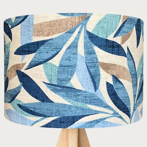 Può includere: Un paralume bianco con un motivo a foglie blu e marroni. Il paralume è cilindrico e ha un tessuto strutturato.