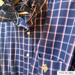 May include: A navy blue button-down shirt featuring a white and red plaid pattern. The shirt includes a collar, a front pocket with an embroidered gold logo of a person on a horse, and white buttons. The text STYLE NO. 046 is visible at the bottom.
