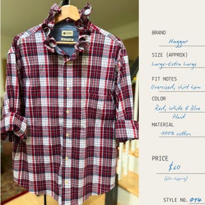 Puede incluir: Una camisa a cuadros roja, blanca y azul con cuello con volantes. La camisa de manga larga está hecha de 100% algodón y tiene un ajuste holgado. La camisa está abotonada y colgada de una percha de madera.
