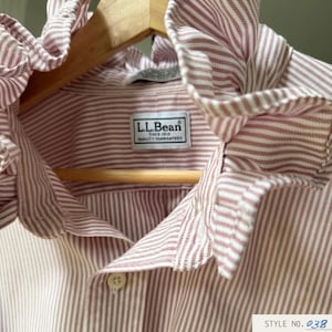 Peut inclure: Une chemise à manches longues avec un motif à rayures verticales blanches et bordeaux, dotée d'un col à volants et d'une fermeture boutonnée. L'étiquette intérieure indique L.L.Bean Since 1912 Quality Guaranteed. Une étiquette indique STYLE NO. 038.