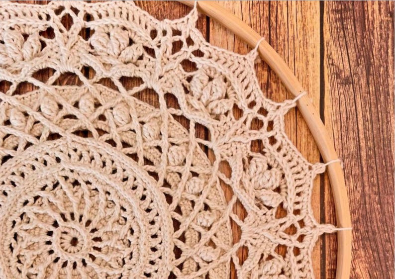 Peut inclure: Attrape-r&ecirc;ves en crochet fait &agrave; la main, de couleur cr&egrave;me, avec des motifs ajour&eacute;s complexes. Le design circulaire est suspendu dans un cerceau en bois naturel. L'artisanat est pr&eacute;sent&eacute; sur un fond en bois.