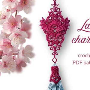 Puede incluir: Un charm de encaje de ganchillo burdeos con borla, sobre un fondo blanco. El charm tiene un diseño intrincado y está acompañado de una rama de flores de cerezo rosas. El texto dice "Lace charm crochet PDF pattern."