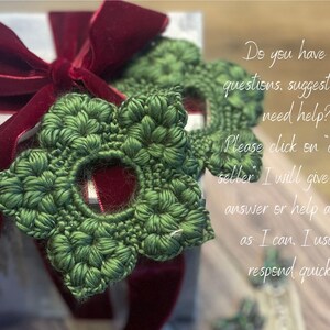 May include: A gift box with a silver and white wrapping, adorned with a deep red velvet bow. Two green, crocheted star-shaped ornaments are placed on top. The image includes text asking for questions.