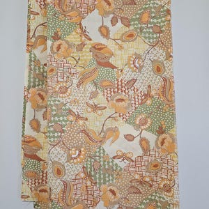 May include: A rectangular piece of fabric featuring a patchwork-style print with an off-white background. The pattern consists of alternating geometric sections in sage green, tan, and orange, decorated with floral motifs, butterflies, and paisley.