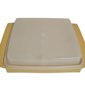 May include: A square, light yellow plastic storage container with a matching, slightly translucent, off-white lid. The container features integrated side handles and a flat, smooth surface design, providing a simple and functional kitchen storage solution.