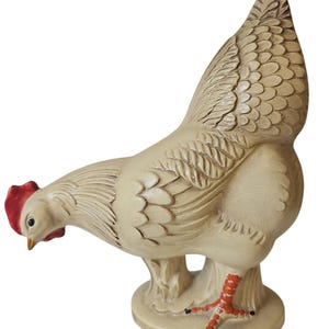 May include: A cream-coloured ceramic hen figurine with a red comb and feet. The hen features detailed feather patterns and stands on a round base. The beak is yellow and the eyes are black.