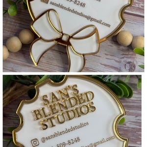 May include: A white and gold business card with the text "SAN'S BLENDED STUDIOS". The card has a gold border and a bow design. Contact information includes an Instagram handle, phone number, and email address.