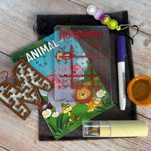 May include: A black drawstring bag containing an animal-themed activity book, a clear plastic grid board with red lines, a wooden letter M maze, a purple marker, a multi-coloured silicone fidget toy, a small orange container, and a clear tube of crayons.
