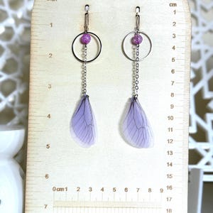 May include: Purple and silver dangle earrings with a small purple glitter bead and a delicate chain. The earrings feature a translucent purple wing design.