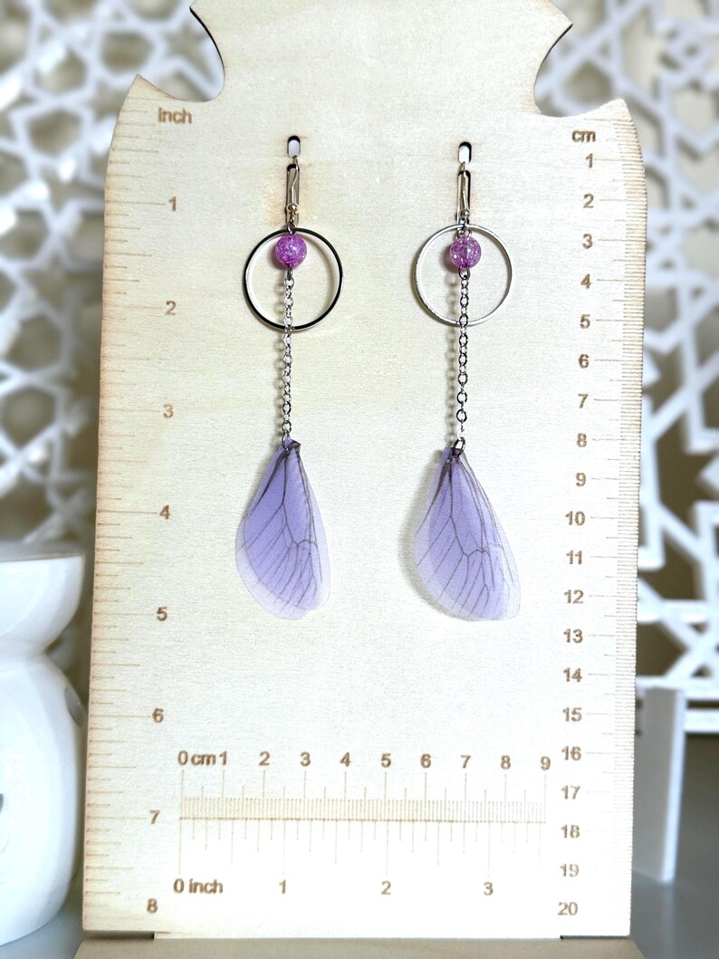 May include: Purple and silver dangle earrings with a small purple glitter bead and a delicate chain. The earrings feature a translucent purple wing design.