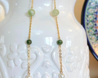 May include: A pair of long gold chain earrings with green and white beads. The earrings have a simple design and are perfect for everyday wear.