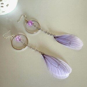 May include: A pair of dangle earrings with a silver hoop and chain, a purple glitter bead, and a delicate purple butterfly wing charm.
