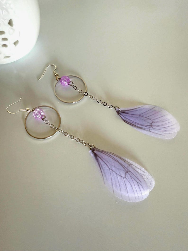 May include: A pair of dangle earrings with a silver hoop and chain, a purple glitter bead, and a delicate purple butterfly wing charm.