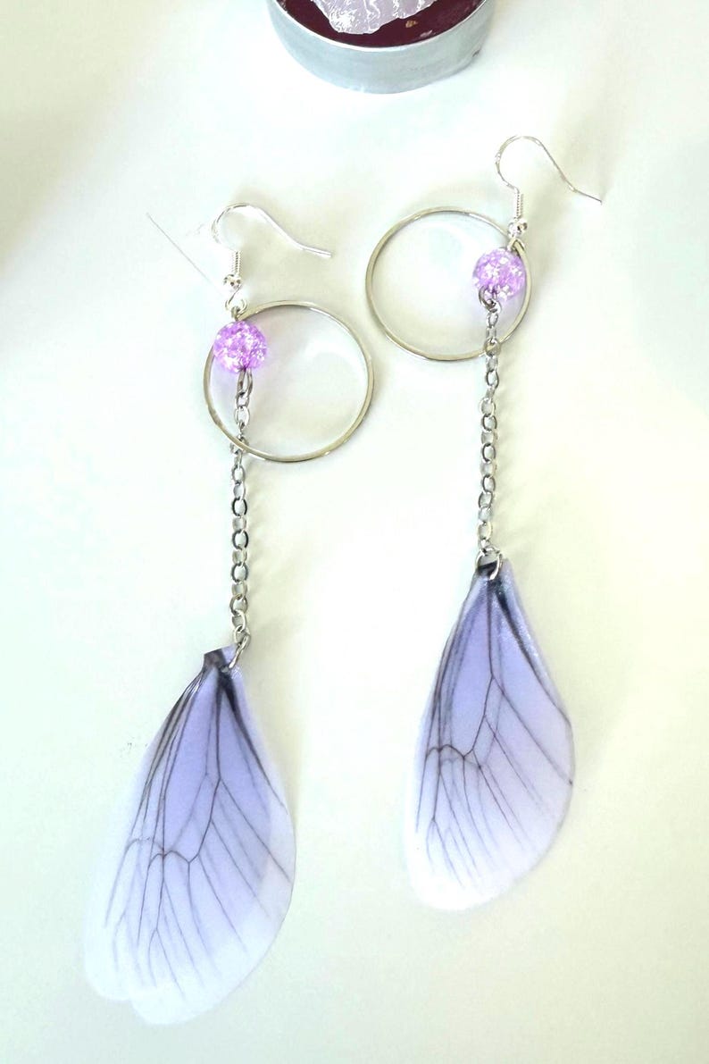 May include: A pair of silver earrings with a purple bead and a delicate, translucent, white and purple wing charm.