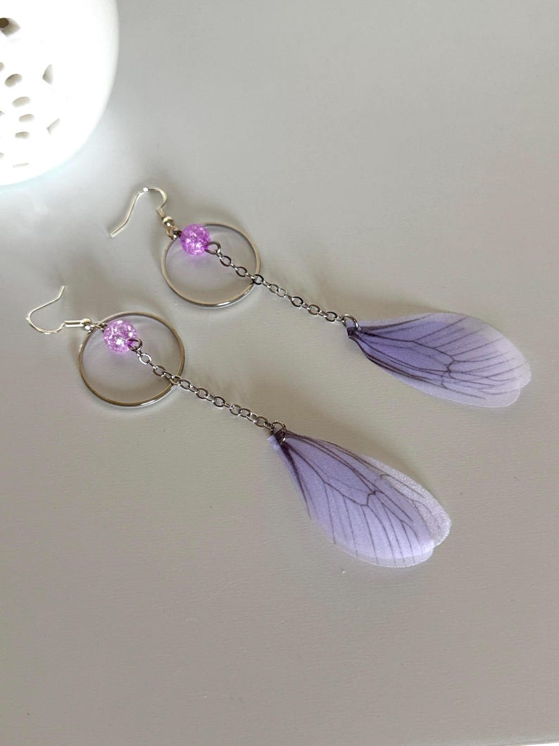 May include: A pair of dangle earrings with a silver hoop, a purple bead, and a delicate purple butterfly wing charm.