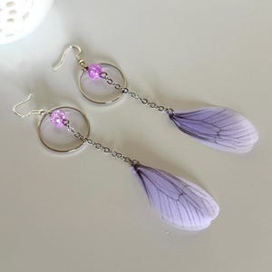 May include: A pair of dangle earrings with a silver hoop and chain, a purple bead, and a delicate purple butterfly wing charm.