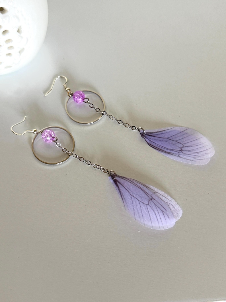 May include: A pair of dangle earrings with a silver hoop and chain, a purple bead, and a delicate purple butterfly wing charm.