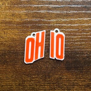 May include: Two white charms with red lettering spelling "OH" and "IO".