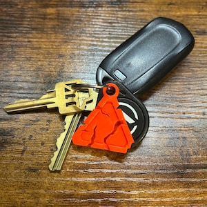 May include: A set of keys with a bright orange triangular keychain. The keychain has a black and white logo on it.