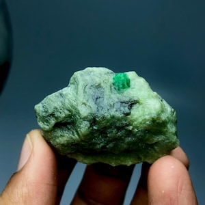 Peut inclure: Une émeraude brute non taillée. L'émeraude brute est d'un vert vif, avec une surface légèrement texturée. La pierre est mise en valeur sur un fond sombre, soulignant sa beauté naturelle. Une pierre précieuse naturelle.