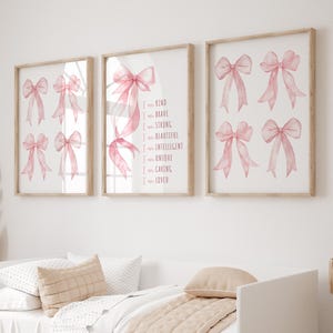 May include: Three framed prints with watercolor pink bows. The center print has the text "I am kind, brave, strong, beautiful, intelligent, unique, caring, loved." The frames are light brown, and the background is white.