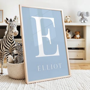 May include: A light blue framed print with a white letter E and the name Elliot in white text.