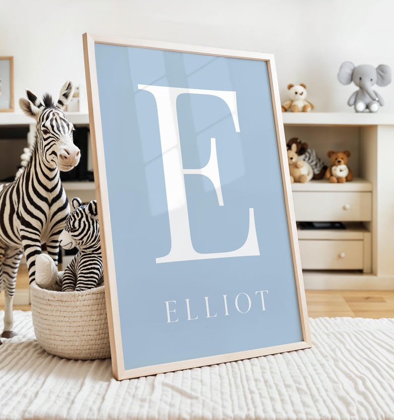 May include: A light blue framed print with a white letter E and the name Elliot in white text.