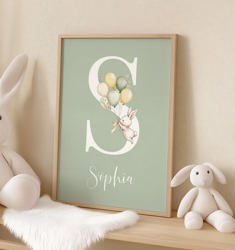 K&ouml;nnte beinhalten: Ein gerahmter Druck mit hellgr&uuml;nem Hintergrund, der einen gro&szlig;en wei&szlig;en Buchstaben "S" zeigt. Eine Aquarellillustration eines Hasen, der Ballons h&auml;lt, ist in den Buchstaben integriert. Der Name "Sophia" ist darunter in Kursivschrift geschrieben.