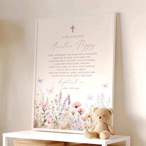 Op de afbeelding: Een ingelijste print met een bloemenontwerp en de tekst "A Prayer For Amelia Poppy". De print bevat een kruis en vlinders. Een kleine teddybeer staat op een witte plank.