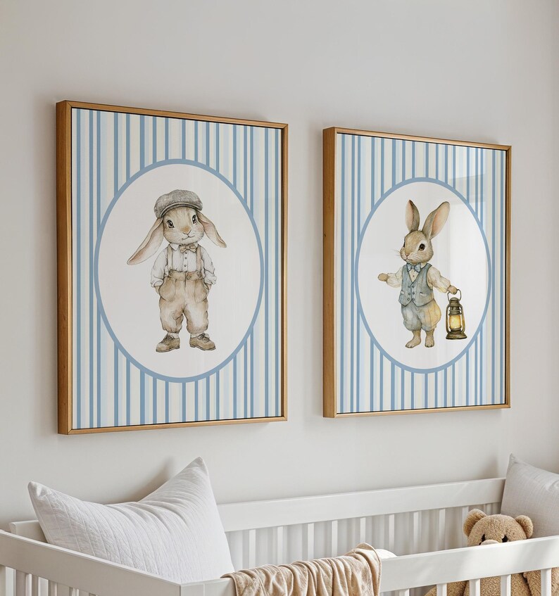 May include: Two framed prints with blue and white striped backgrounds. Each print features a circle with a cartoon bunny wearing clothes. One bunny is wearing a cap and the other is holding a lantern.
