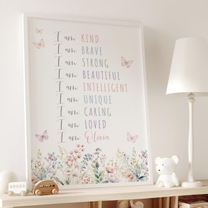 以下が含まれることがあります： I am KIND, I am BRAVE, I am STRONG, I am BEAUTIFUL, I am INTELLIGENT, I am UNIQUE, I am CARING, I am LOVED, I am Oliviaというテキストが書かれた額入りアートプリント。パステルカラーの蝶と下部の花柄のボーダーが特徴です。