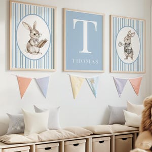 May include: Three framed prints with a blue and white striped background. The center print features a large white letter "T" on a light blue background with the name "THOMAS" printed below. The prints on either side feature a watercolor illustration of a rabbit wearing glasses and holding a book on the left and a rabbit holding a pocket watch on the right.