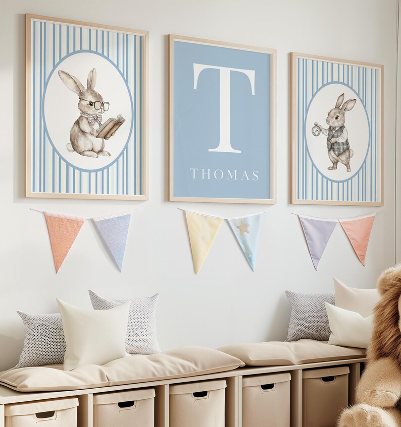 May include: Three framed prints with a blue and white striped background. The center print features a large white letter "T" on a light blue background with the name "THOMAS" printed below. The prints on either side feature a watercolor illustration of a rabbit wearing glasses and holding a book on the left and a rabbit holding a pocket watch on the right.