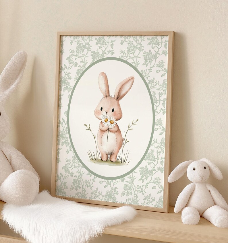 K&ouml;nnte beinhalten: Ein gerahmter Druck mit einer Aquarellillustration eines hellrosa Hasen, der G&auml;nsebl&uuml;mchen h&auml;lt. Der Hase befindet sich in einem ovalen Rahmen, vor einem floral gemusterten Hintergrund. Der Holzrahmen verleiht diesem charmanten Kunstwerk eine nat&uuml;rliche Note, ideal f&uuml;r die Kinderzimmerdekoration.