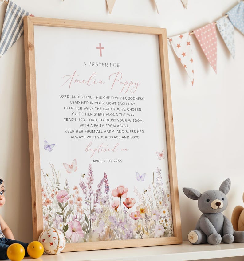 Op de afbeelding: Een ingelijste print met een licht houten frame. De print toont een gebed voor "Amelia Poppy" met een bloemenontwerp in zachte roze en paarse tinten. Vlinders en een kruis zijn ook inbegrepen. De woorden "gedoopt op 12 april 20XX" staan onderaan.
