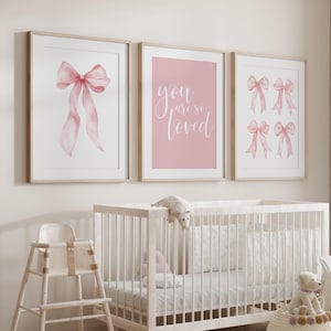 May include: Three framed prints with watercolor bow illustrations and the text "you are so loved" in a nursery setting. The prints feature pink bows and a pink background. A white crib and high chair are in the foreground.