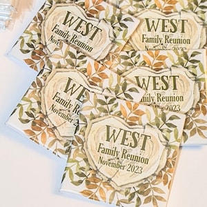 May include: A set of four square-shaped magnets with a wood grain design and green and brown leaves. The magnets feature the text "WEST Family Reunion" and the month and year of the reunion.
