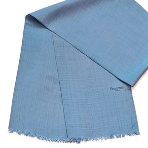 May include: A pale blue scarf with a textured weave and fringed edges. The scarf is folded, showing a glimpse of the underside. The brand name "Brummell PARIS" is printed in the lower right corner.