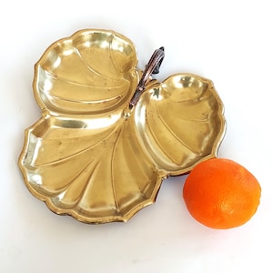 Puede incluir: Una bandeja de servir de metal dorado con forma de hoja con tres secciones y un asa de cobre.