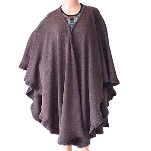 May include: A brown poncho with a V-neck design and a layered, ruffled hem. The poncho is draped over a mannequin, revealing a glimpse of a patterned top underneath. The fabric appears to be a soft knit.