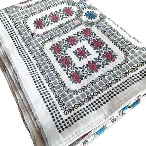May include: A white tablecloth with a black and gold embroidered floral pattern. The tablecloth has a fringed edge and is folded in half.