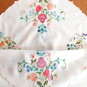 May include: White embroidered tablecloth with a scalloped edge and floral designs in shades of pink, blue, green, and yellow.